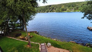 Vista de un lago con una terraza de madera que conduce a un área verde con mobiliario exterior.