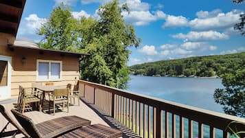 Une terrasse en bois, agréée de mobilier d’extérieur, qui offre une vue sur un lac et est entourée d’arbres.