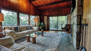 Un salon spacieux doté d’un plafond en bois, de grandes fenêtres, d’une cheminée en pierre et d’un coin salon confortable.