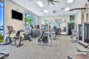 A gym with various exercise equipment, large windows, and a ceiling fan.