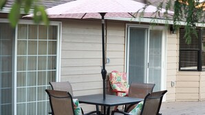 Un patio con una mesa, cuatro sillas, una sombrilla y un ventanal corredera.