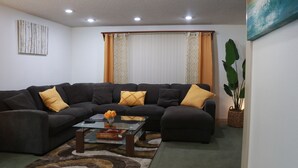 Una sala de estar con un sofá modular, una mesa de centro de vidrio y una planta grande.