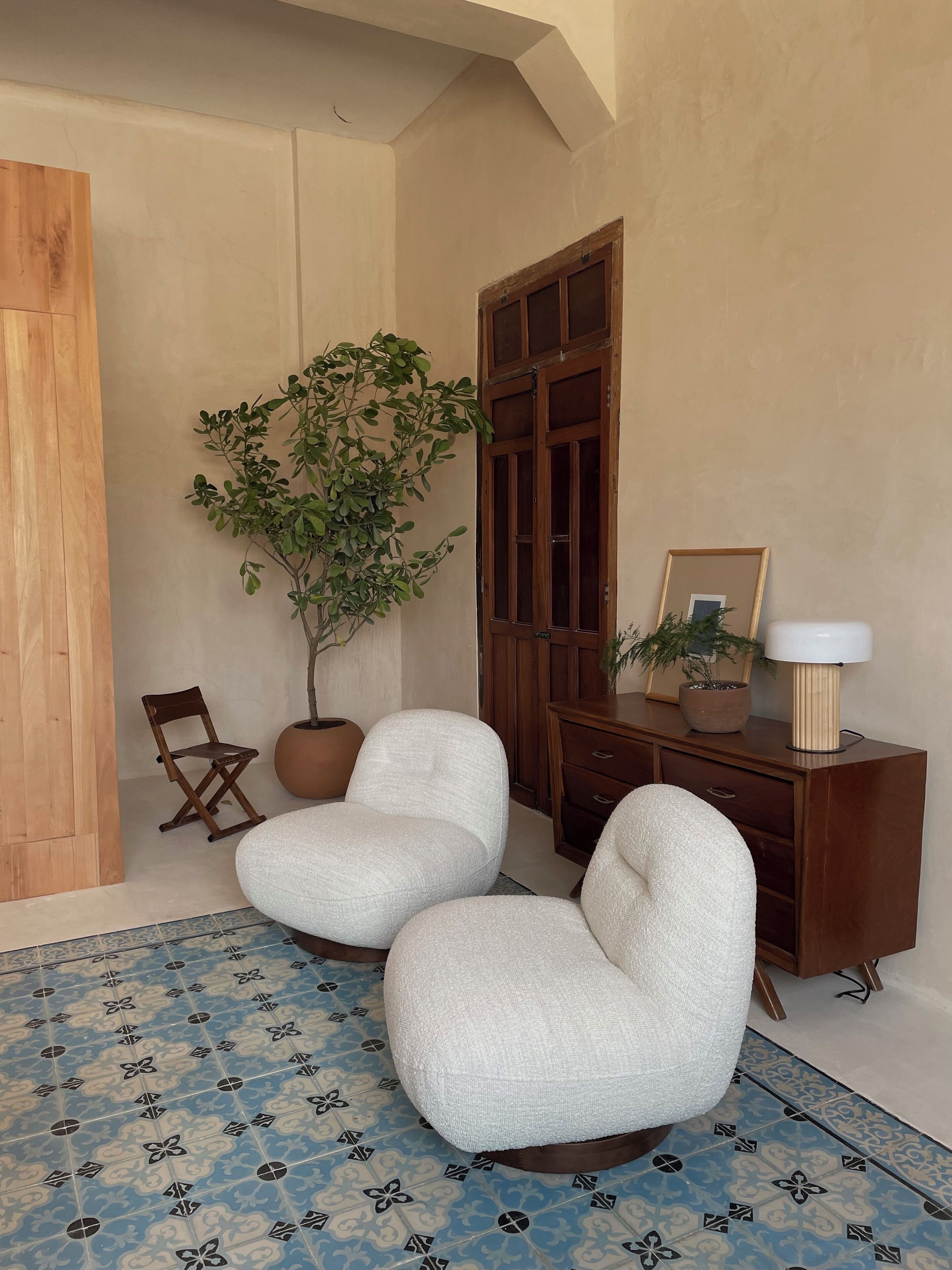 A room with two white armchairs, a wooden cabinet, a potted plant, and a patterned rug.