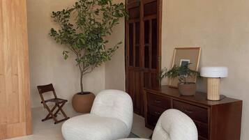 A room with two white armchairs, a wooden cabinet, a potted plant, and a patterned rug.
