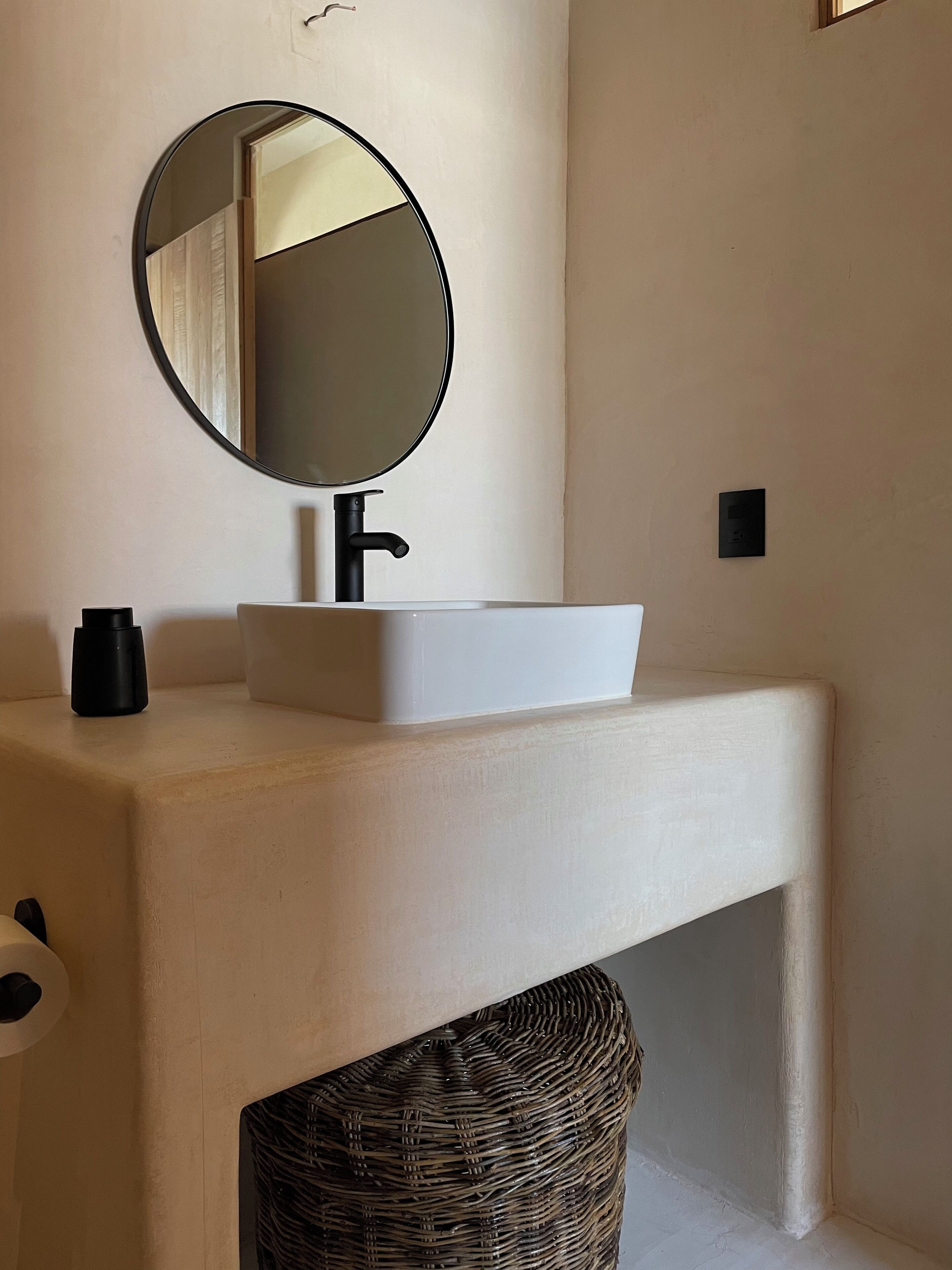 A bathroom with a white sink, black faucet, and a round mirror.
