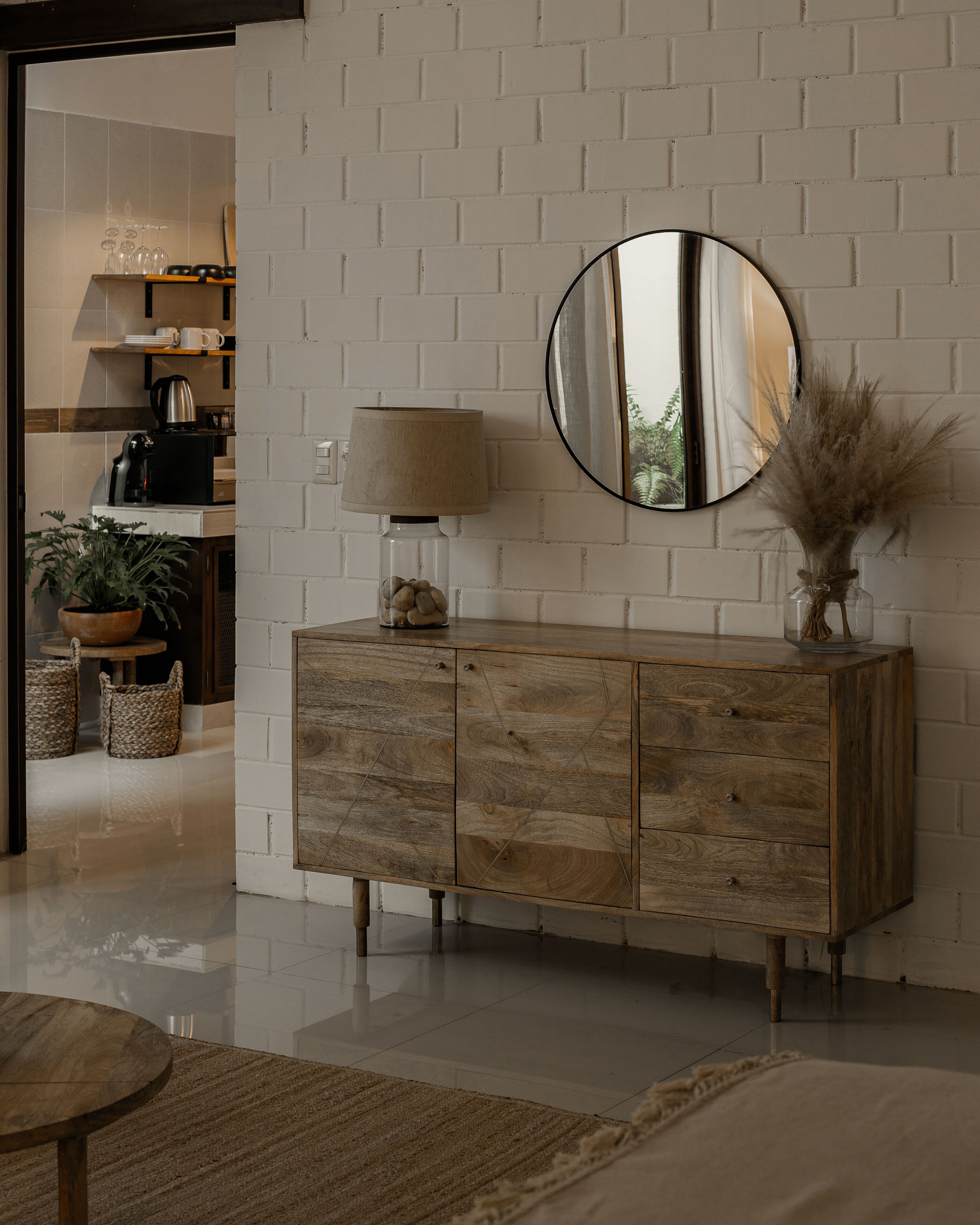 Una sala de estar moderna con un mueble de madera, un espejo redondo, una lámpara y una planta en maceta.
