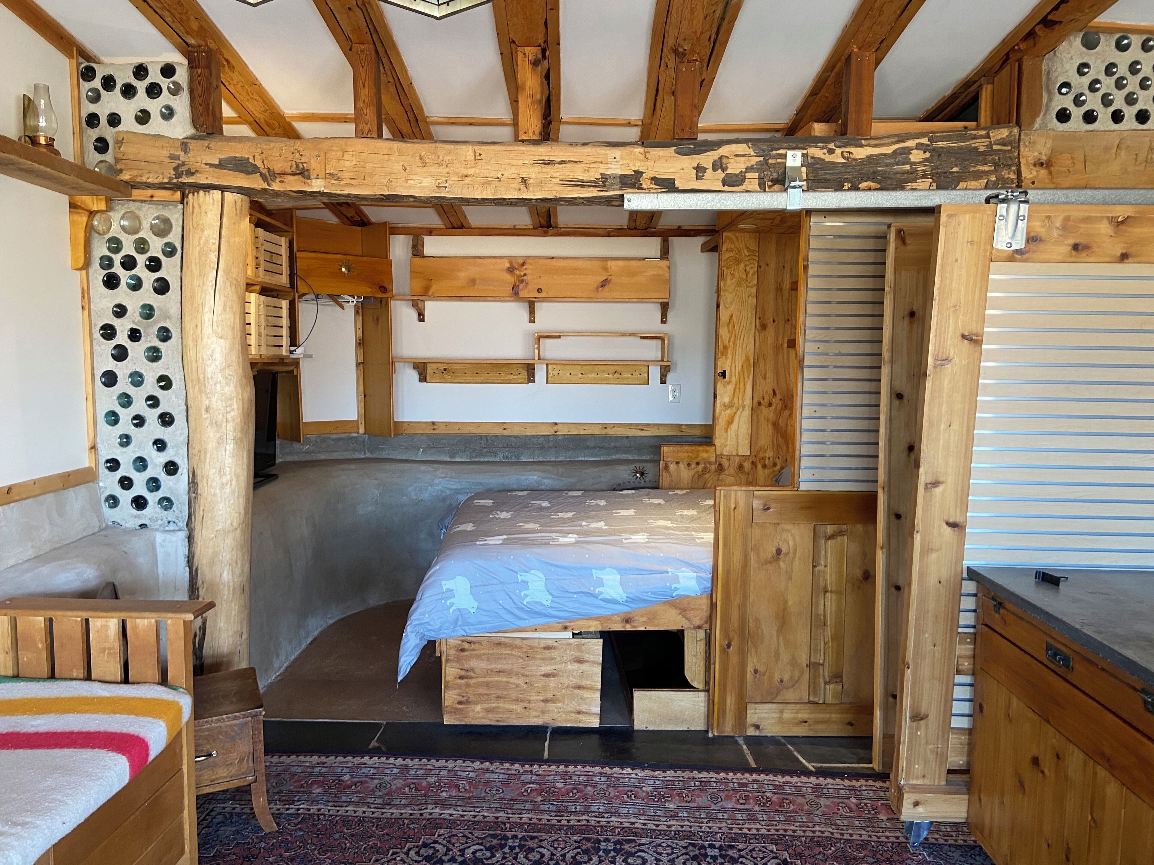 A rustic wooden room with a bed, a small table, and a bench.