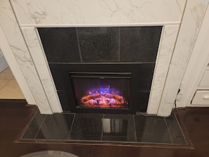 A fireplace with a glass screen, surrounded by white marble tiles and dark stone accents. - Victoria home near to downtown  oakland!!! (Oakland)