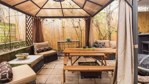 Un patio couvert avec une table en bois, des bancs et des sièges rembourrés.