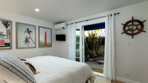 Un dormitorio con cama, televisor y vista a un jardín a través de una puerta corrediza.