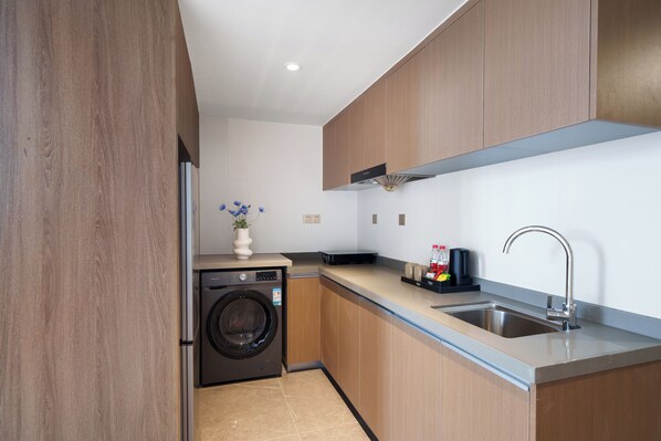 A modern kitchen with wooden cabinets, a built-in washing machine, a sink, and a countertop with a vase of flowers.