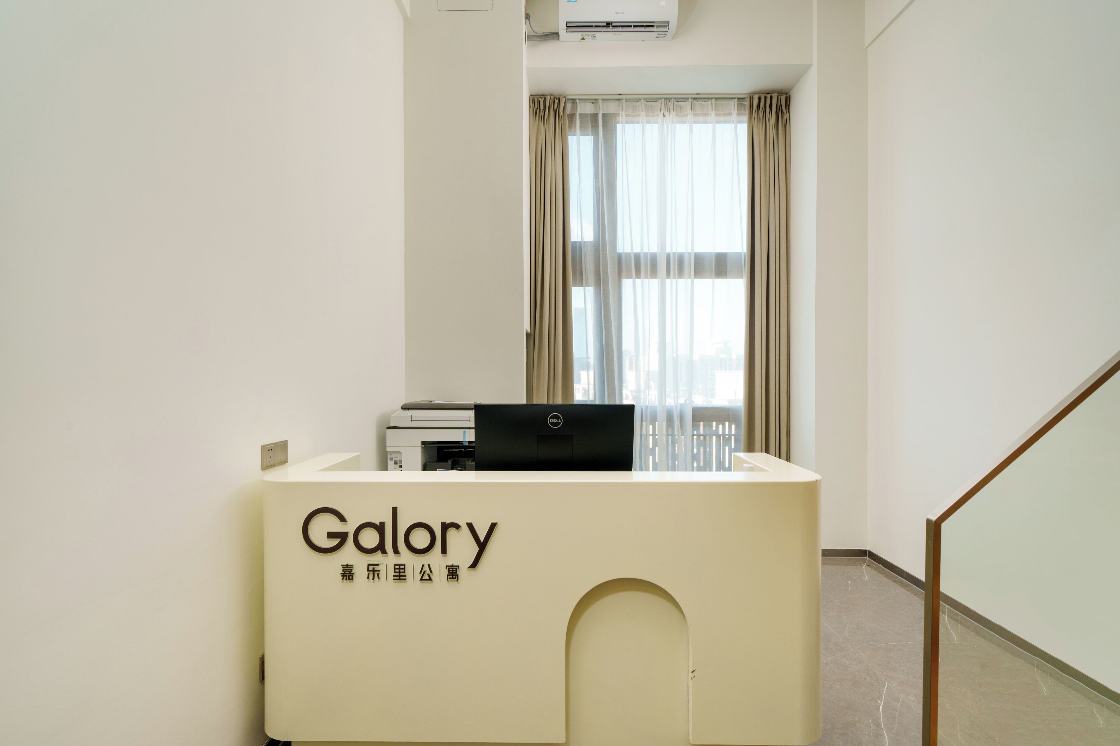 A reception desk with a laptop and a printer, a window with curtains, and a staircase.