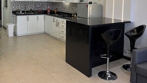 A modern kitchen with white cabinets, a black countertop, and two black bar stools. - Luxury apartments  (La Romana)