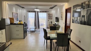 A modern kitchen with a refrigerator, a dining area with a table and chairs, and a living space with a sofa and a TV. - Luxury apartments  (La Romana)