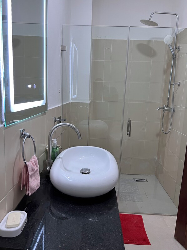 Un baño con un lavamanos blanco, cabina de ducha de vidrio y una alfombra roja en el suelo.