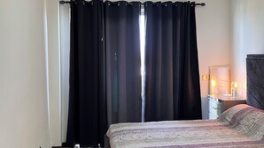 A bedroom with a bed, a nightstand, a lamp, and a window with curtains. - Luxury apartments  (La Romana)