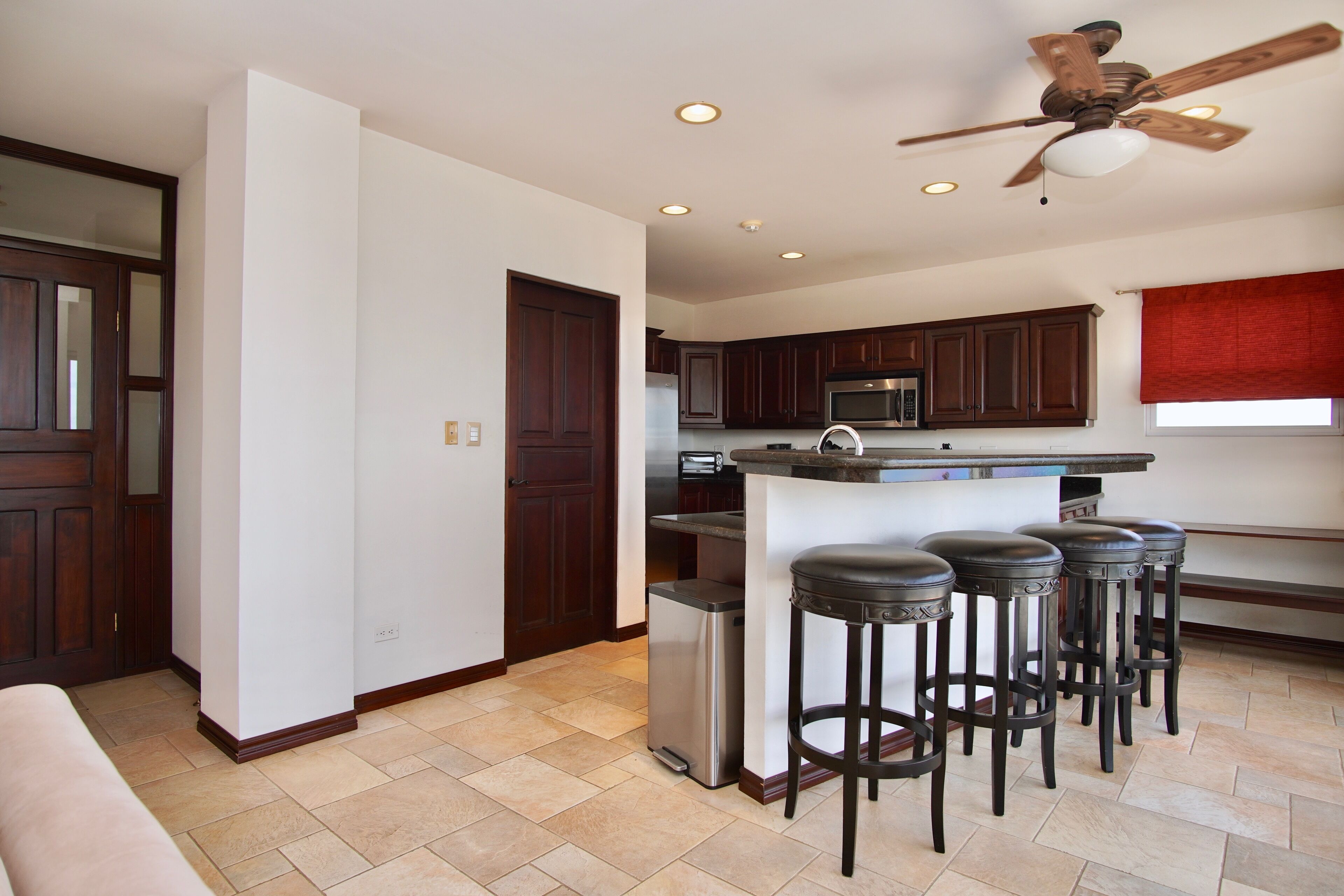 A modern kitchen with dark wooden cabinets, a stainless steel refrigerator, and a bar area with stools.