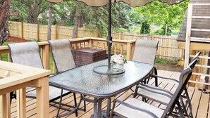 Un patio exterior con una mesa redonda de vidrio, sillas acolchadas y un paraguas grande.