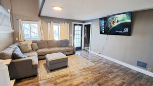 Una sala moderna con un sofá modular, un reposapiés gris y un televisor de pantalla plana montado en la pared.