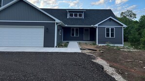 A two-story house with a garage, a covered driveway, and a landscaped front yard. - Peaceful newly built home between Fish Creek and Ephraim, WI. 3 bed/ 2 bath. (Fish Creek)