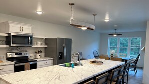 A modern kitchen with a marble countertop, stainless steel appliances, and a large island with bar stools. - Peaceful newly built home between Fish Creek and Ephraim, WI. 3 bed/ 2 bath. (Fish Creek)