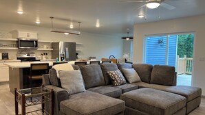A modern living room with a sectional sofa, a glass coffee table, and a dining area with a kitchen in the background. - Peaceful newly built home between Fish Creek and Ephraim, WI. 3 bed/ 2 bath. (Fish Creek)