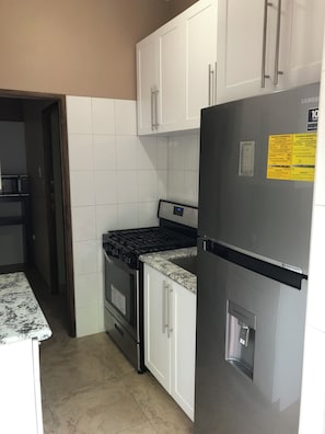A kitchen with white cabinets, a stainless steel refrigerator, a stove, and a microwave.