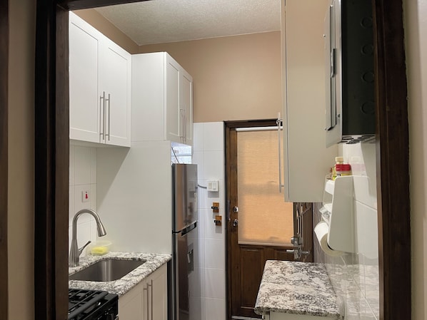 A compact kitchen with white cabinets, a stainless steel refrigerator, a sink, and a stove.