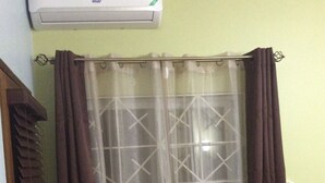 Een badkamer met douchegordijn, een raam met geometrisch patroon en een airconditioner aan de muur.
