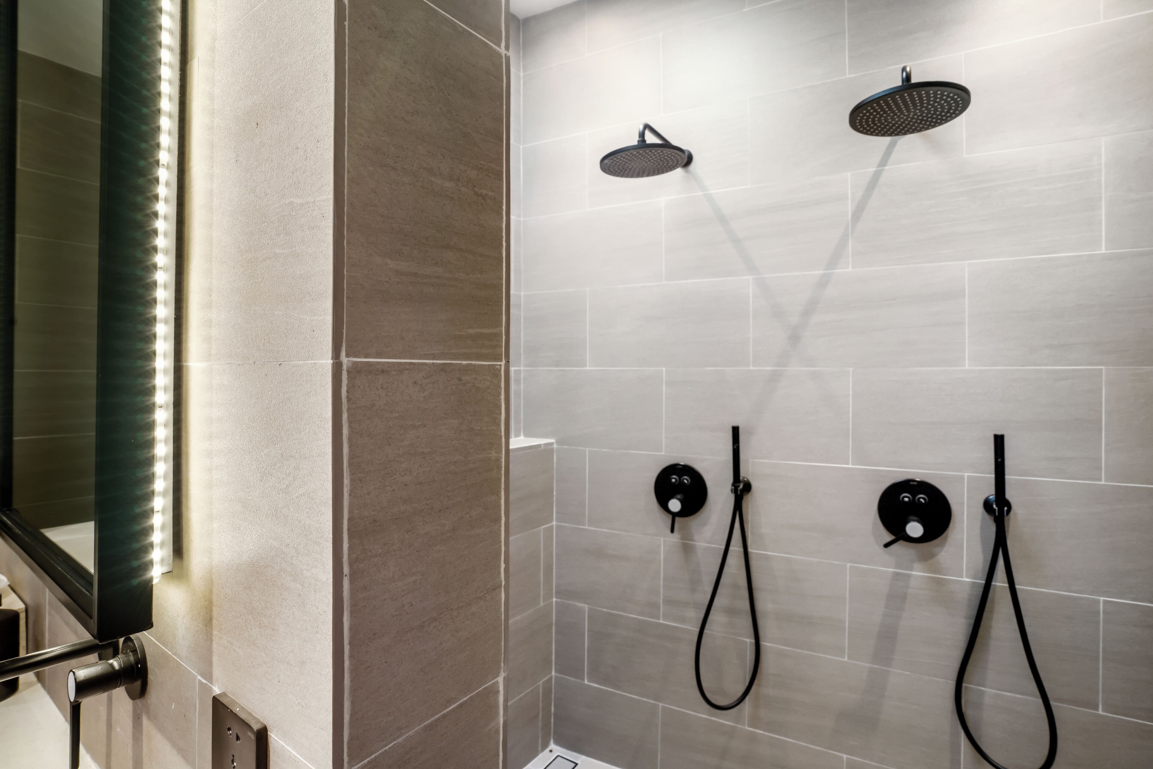 Un área de ducha moderna con dos cabezales de ducha superiores y dos cabezales de ducha manuales montados en la pared.