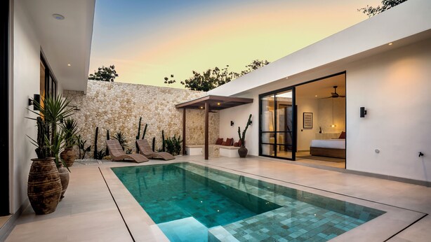 A modern pool area with a stone wall, lounge chairs, and a glass-enclosed room with a bed. - Apricot House by Alfred in Bali (Pecatu)