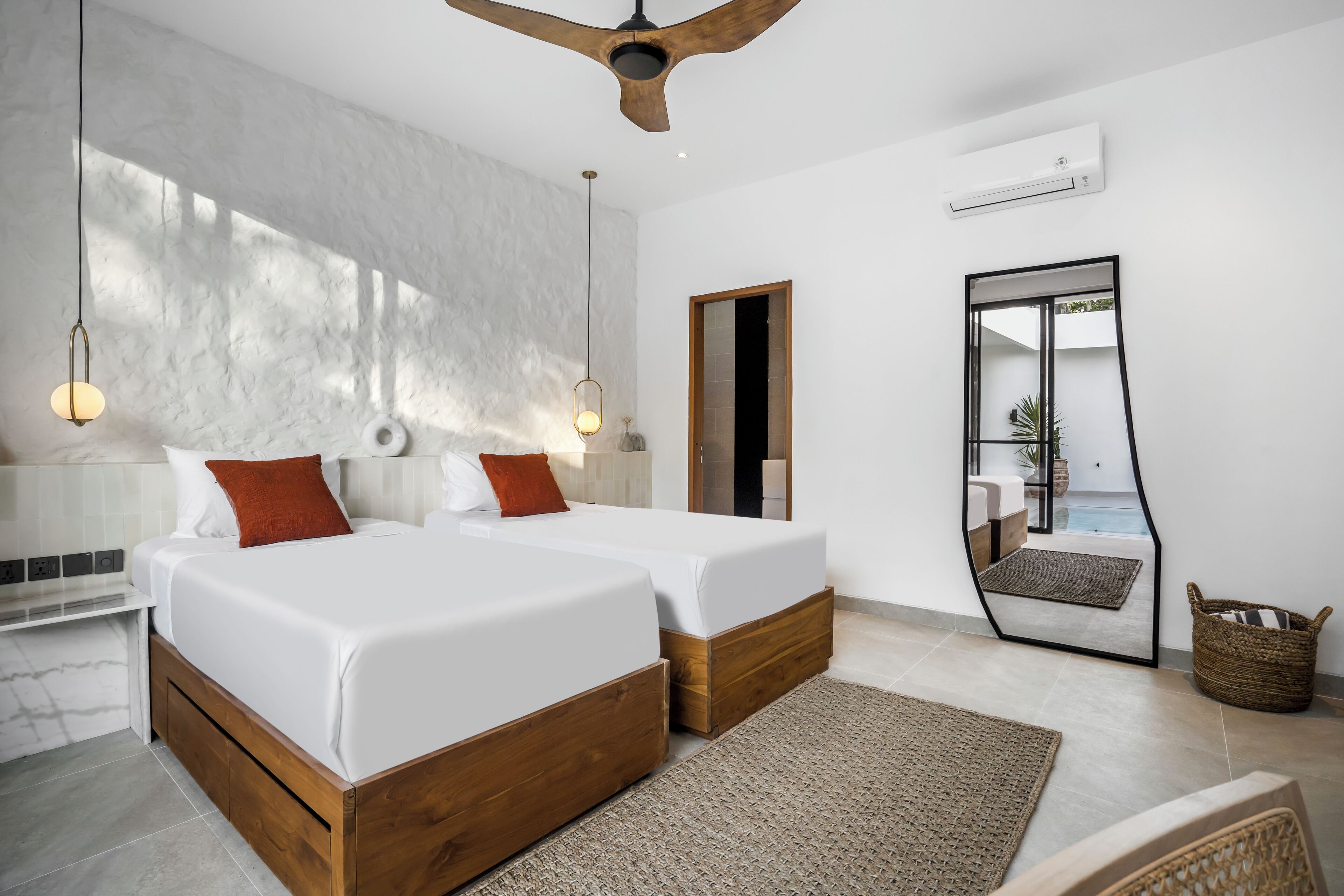 A modern bedroom with two beds, a ceiling fan, and a large mirror reflecting a balcony.