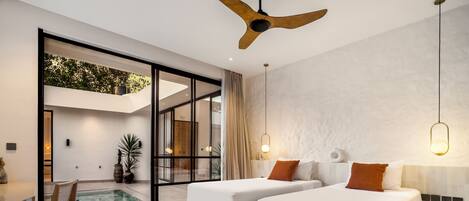 A modern bedroom with two beds, a ceiling fan, a small pool, and a view of greenery outside.