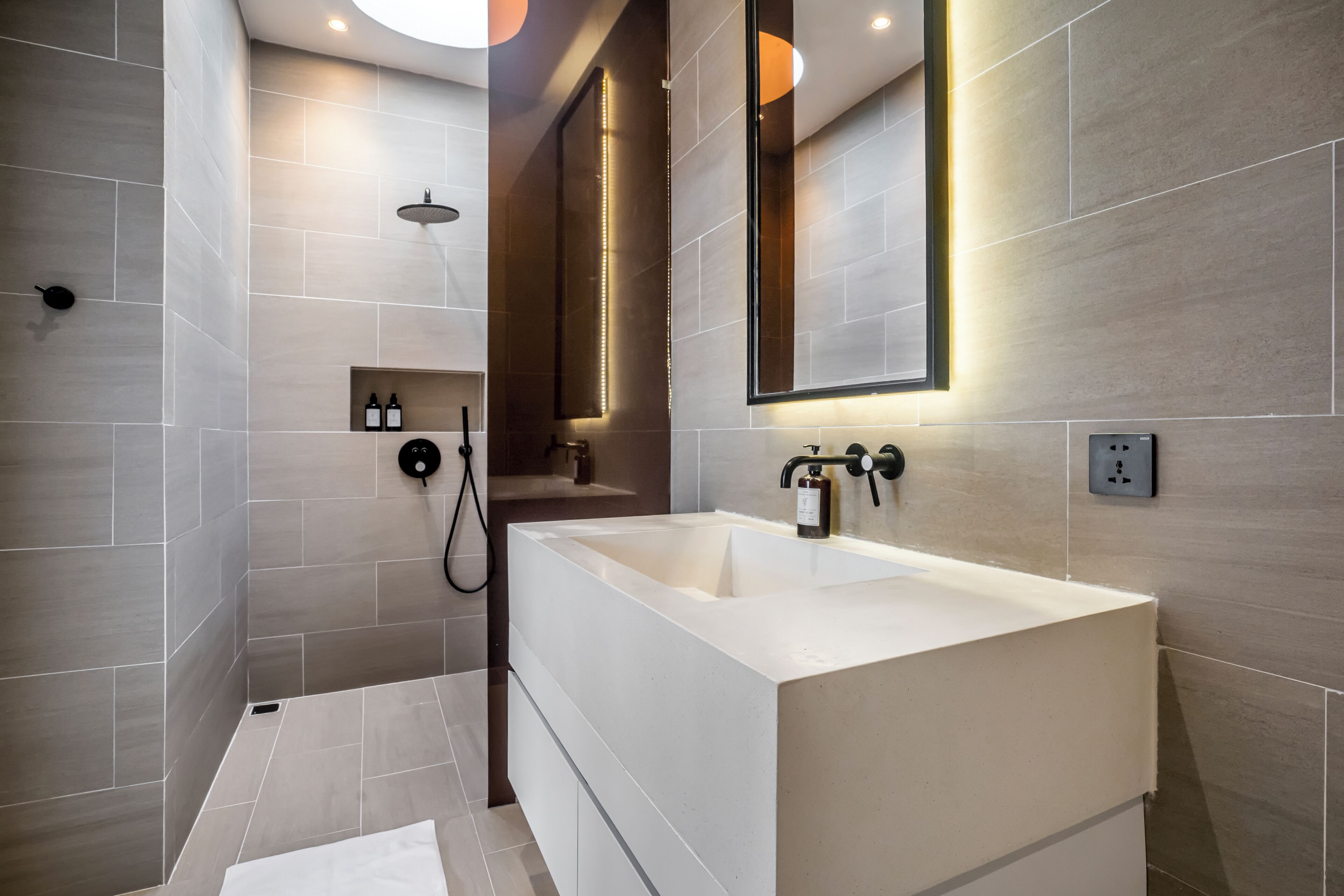 Un bagno moderno con un lavandino bianco di grandi dimensioni, una cabina doccia e uno specchio con illuminazione integrata.