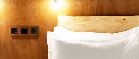 A hotel room with a wooden headboard, a wall-mounted light, and a control panel.