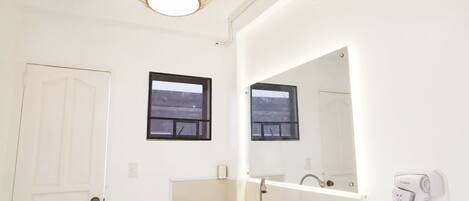 A modern bathroom with a white sink, a mirror, a hanging light fixture, and a hairdryer on the wall.