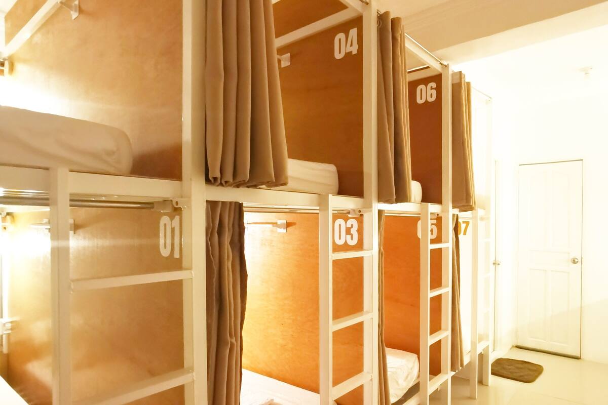 Habitación tipo dormitorio con literas numeradas del 01 al 06, paredes blancas y una puerta al fondo.