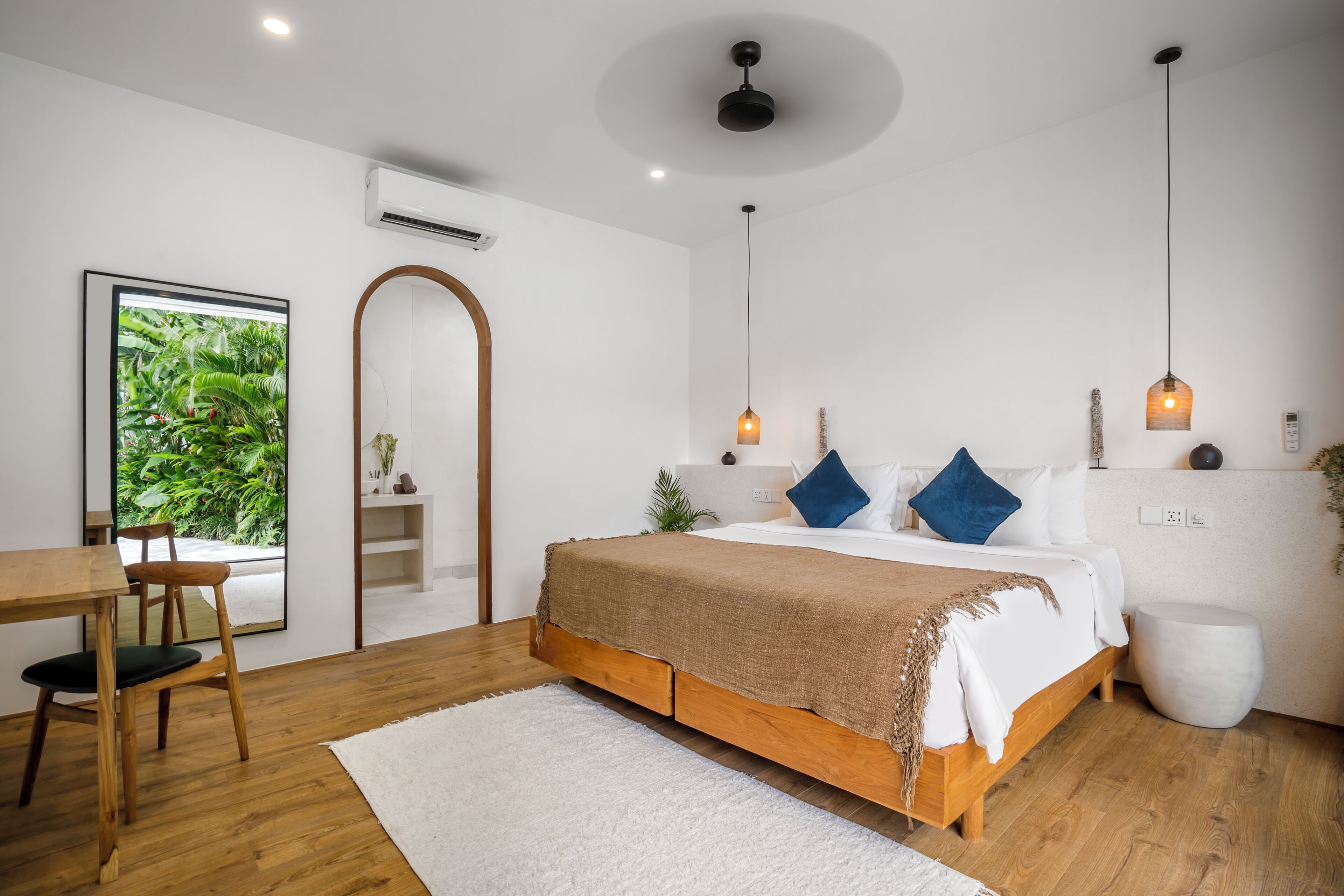 A modern bedroom with a wooden bed, white walls, and a large window with a view of greenery.