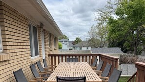 A wooden deck with a table and chairs, a brick wall, and a view of neighboring houses. - Large Home in Quiet Neighborhood (Taylorsville)