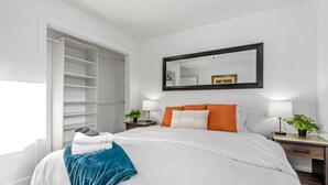 A hotel room with a large bed, a wardrobe, a mirror, and two bedside tables with lamps and plants. - Large Home in Quiet Neighborhood (Taylorsville)