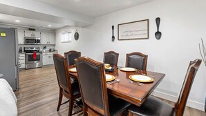 A dining area with a wooden table and chairs, a kitchen in the background, and a framed quote on the wall. - Large Home in Quiet Neighborhood (Taylorsville)