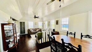 A spacious living room with a wooden dining table, black chairs, a sofa, and a ceiling fan. - Crucian Fusion: Historic charm meets lush beauty in a rare garden oasis in downtown Christiansted! (Christiansted)