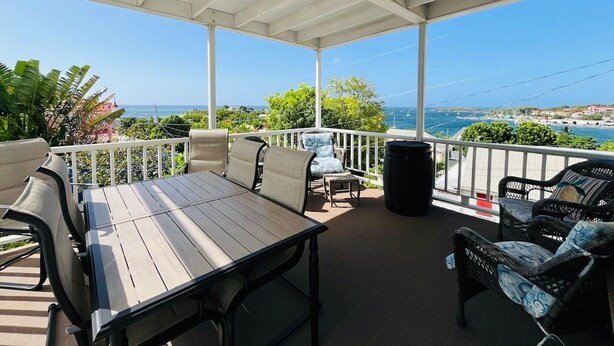 A covered outdoor patio with a table and chairs, a trash can, and a view of the ocean and coastline. - Crucian Fusion: Historic charm meets lush beauty in a rare garden oasis in downtown Christiansted! (Christiansted)