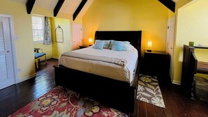 A bedroom with a bed, bedside tables, a chair, and a window. - Crucian Fusion: Historic charm meets lush beauty in a rare garden oasis in downtown Christiansted! (Christiansted)