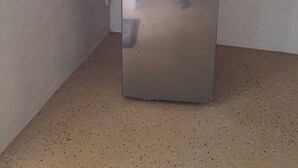 Un frigorifero compatto in acciaio inox posizionato in un angolo di una stanza con pavimento decorato.