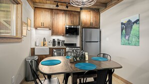 Cucina con mobili in legno, elettrodomestici in acciaio inossidabile e zona pranzo con tavolo e sedie.