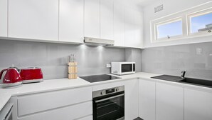 Una cocina moderna con armarios blancos, una campana extractora de acero inoxidable, un microondas, un hervidor rojo y un horno empotrado.