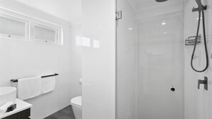 Un baño moderno con cabina de ducha de vidrio, inodoro y tocador con barra para toallas.
