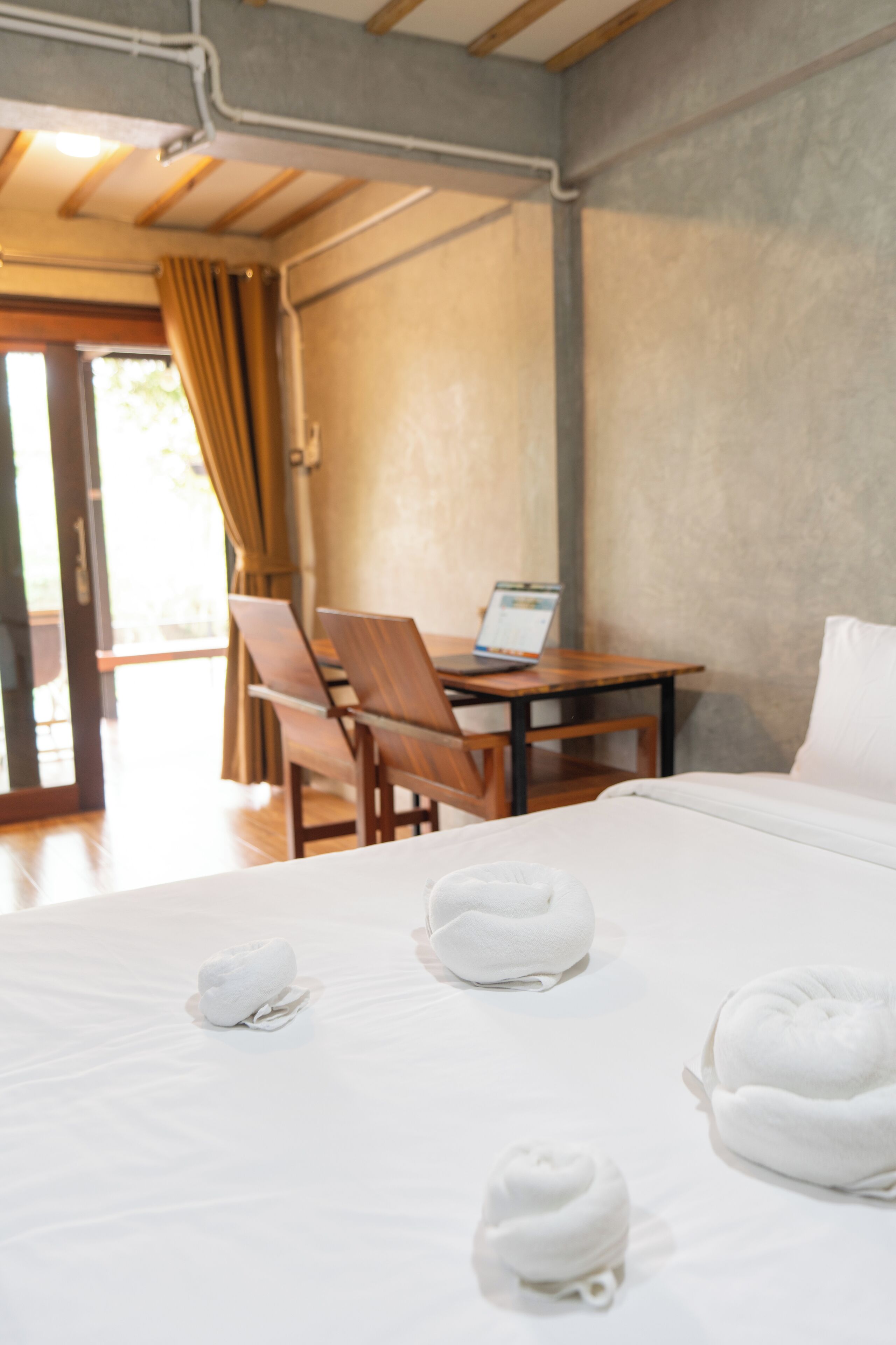 A hotel room with a bed, a desk with a laptop, a chair, and a view of the outdoors.
