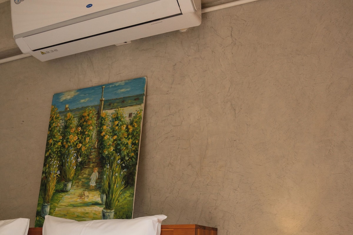 Une chambre à coucher avec un lit en bois, du linge de lit blanc, une table de chevet avec une lampe et un tableau accroché au mur.